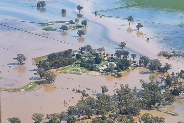An aerial view of a small group of buildings not yet inundated by the surrounding floodwater