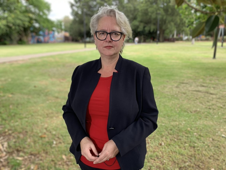 Penny Sharpe standing in a park with a black blazer and red top, glasses