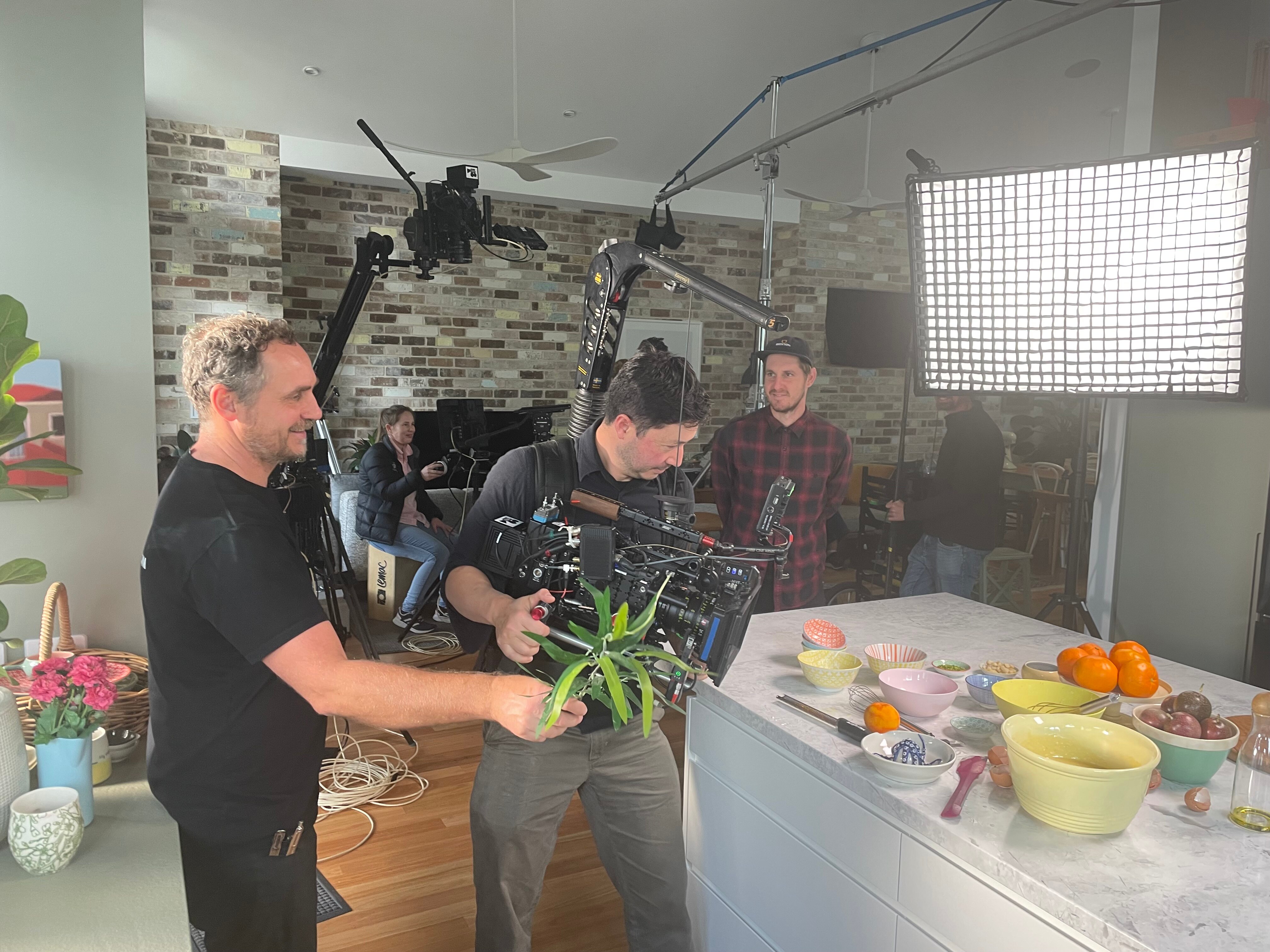 Camera crew filming food on a kitchen bench with a large light in the background.