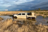 Ute stuck in flood waters west of Mount Isa with RACQ Life Flight helicopter in background.