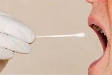 A cotton tipped swab being used to collect a saliva sample from inside a woman's mouth.