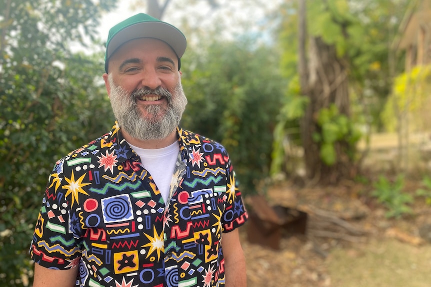 Adrian Ninnes with salt and pepper beard smiling in garden wearing a cap and patterned shirt