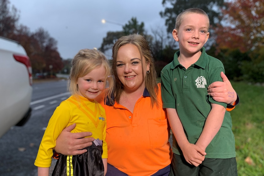 Woman wearing orange shirt with two children. 