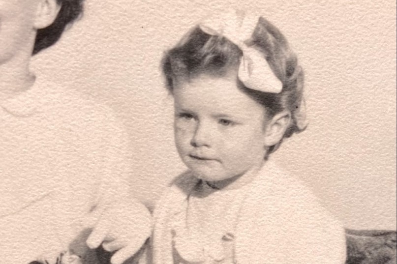 A black and white photo of a young girl with a bow in her hair