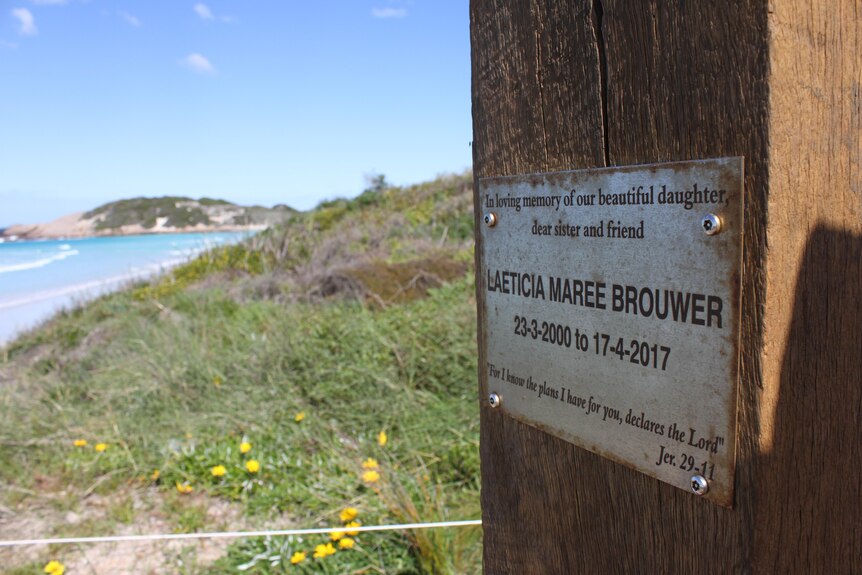 A wooden plaque acknowledging the death of Laeticia Brouwer overlooks the ocean.