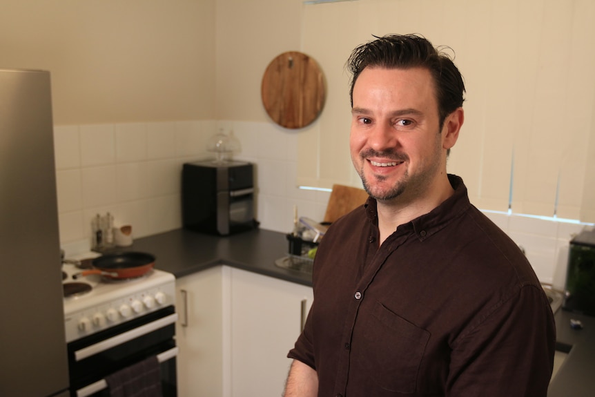 A man with short brown hair and a brown shirt on in a kitchen