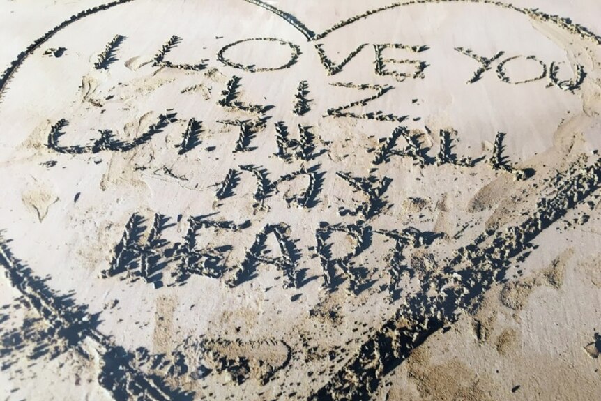 A love heart drawn in the sand with a message inside which reads 'I love you Liz with all my heart'
