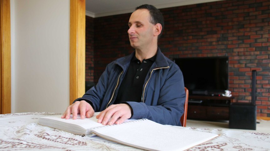 RSB client Michael Zannis reads a book in braille