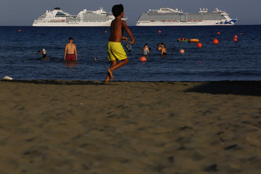 A boy runs on Saint Rafael beach in Cyprus where a number of cruise ships are anchored.