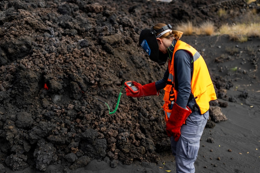 A woman in an orange vests checks a meter with probes stuck in rocks