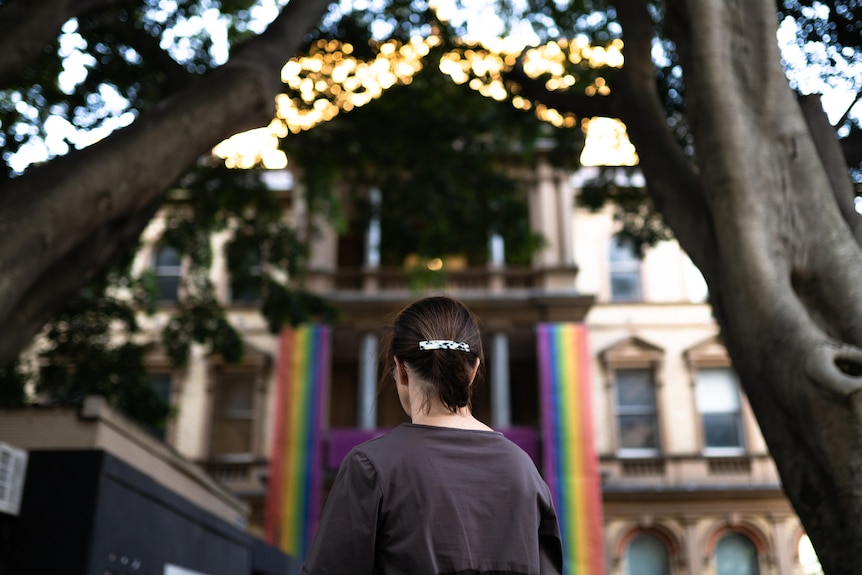 The back of a woman standing in front of a hospital with a colourful rainbow banner