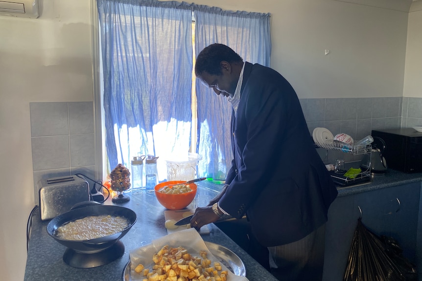 A man cooking in his curtained kitchen. Potatoes are on the menu. 