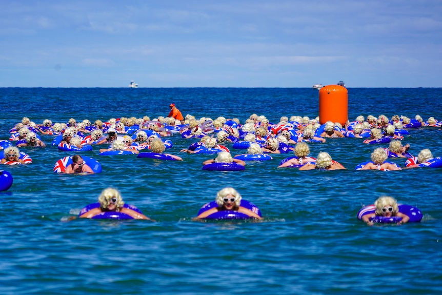 Dozens of people dressed as Marilyn Monroe bobbing in the ocean on blue swim rings