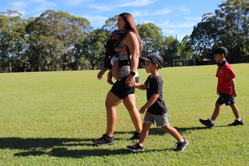 Mum carrying baby in baby carrier and holding boys hand while walking