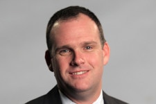 A man with a short dark hair smiling in a professional photograph 