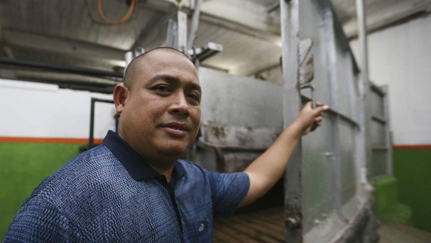 A man shows the inside of a metal restraint cage inside an empty abattoir.