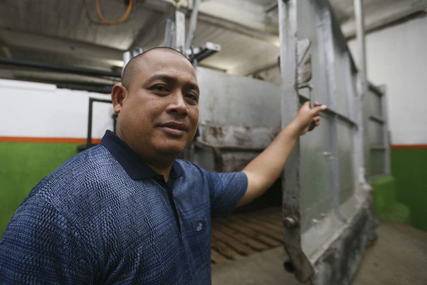 A man shows the inside of a metal restraint cage inside an empty abattoir.