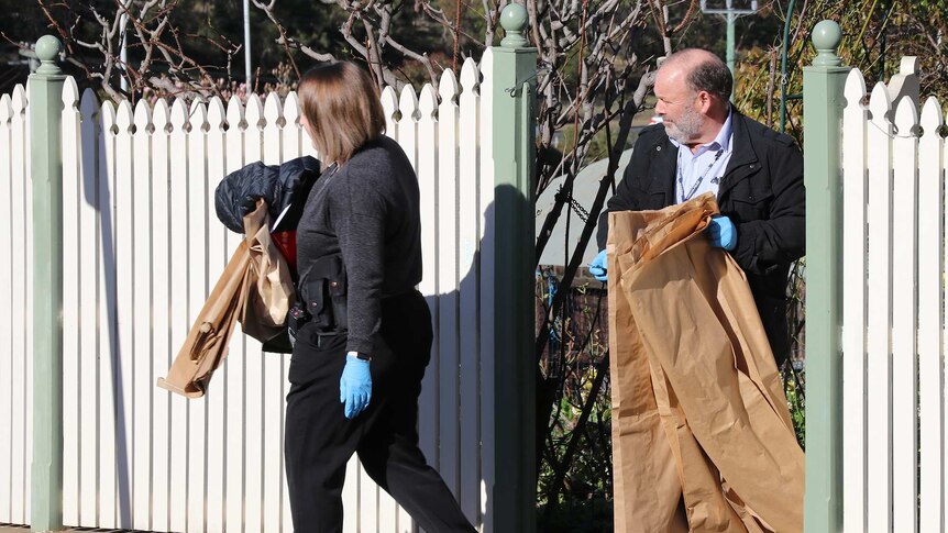 Two people exit a residential property with items wrapped in paper.