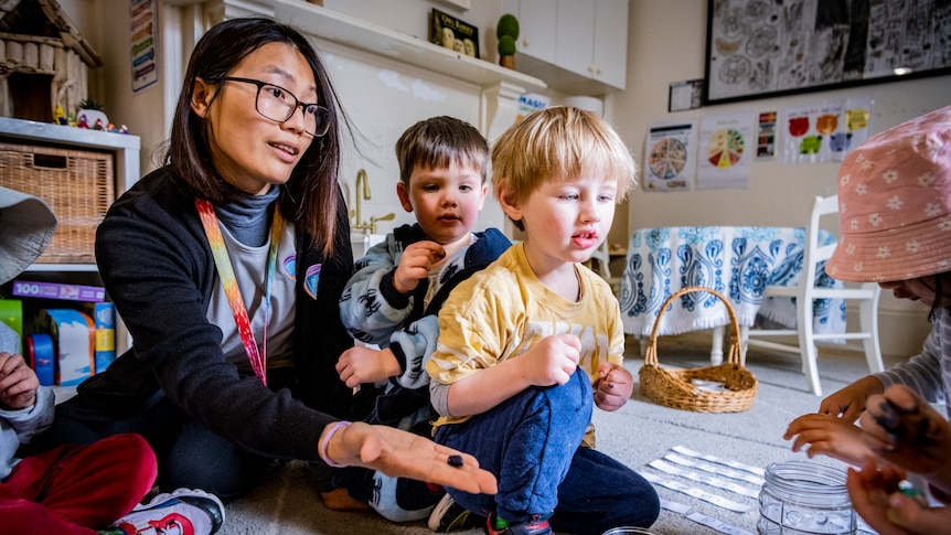 A childcare educator sitting on a mat, playing with kids