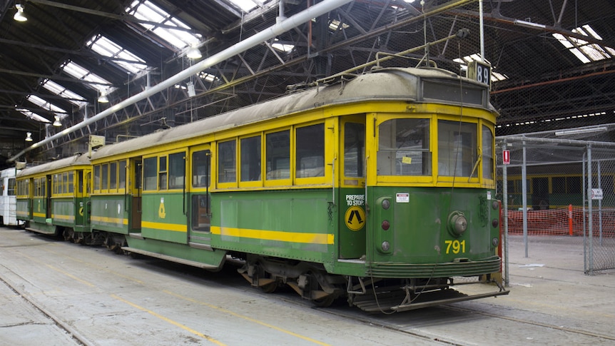 Two old green and yellow trams in a row inside a large warehouse.