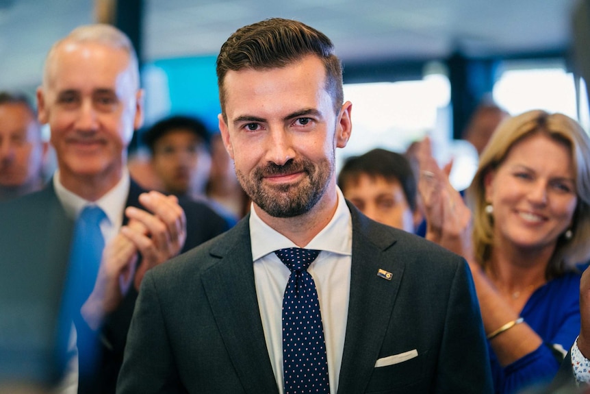 A close up of Zak Kirkup in focus, with a crowd of people blurred in the background.