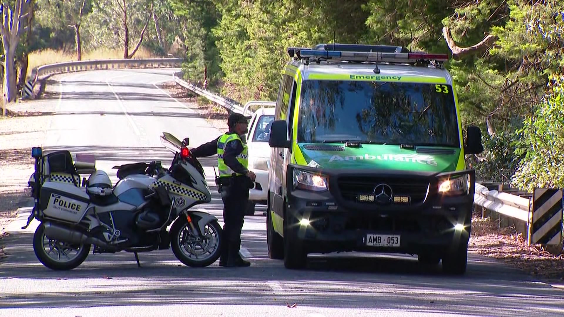 A police officer on the phone walks past a police motorcycle parked in the middle of a road