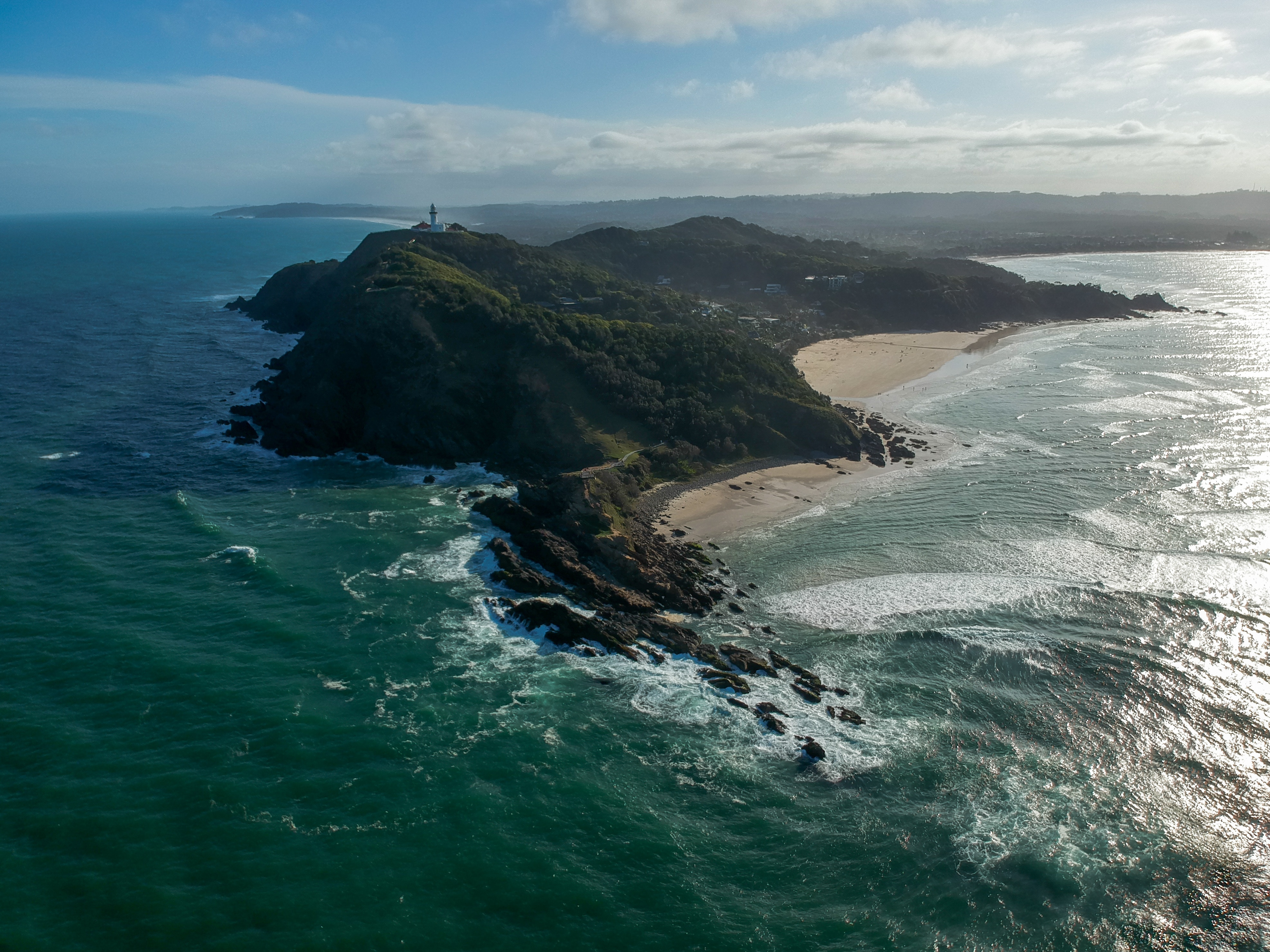 An aerial photo of a rocky headland with lighthouse on the ridge and beach coves. 