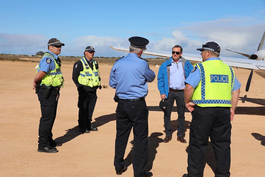The WA Premier gets off a plane standing next to police officers in uniform.  