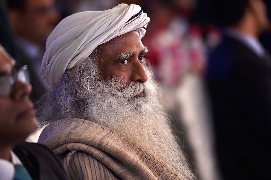Side view of South Asian man with long curly white beard wearing white turban looking into the distance, at a formal event