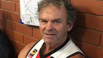 Mullewa Football Club president Mick Wall sits in a changeroom wearing the club's jumper with his arms folded and smiling.