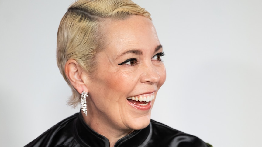 A woman with cropped bleached-blonde hair and long sparkly earrings laughs on the red carpet