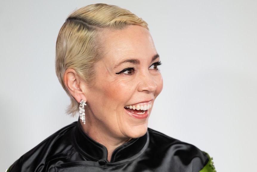 A woman with cropped bleached-blonde hair and long sparkly earrings laughs on the red carpet