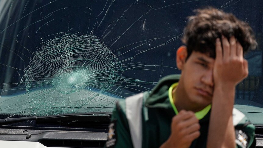 A St John Ambulance worker looks on in front of an ambulance windscreen, which had been smashed by an Ellyse Perry six.