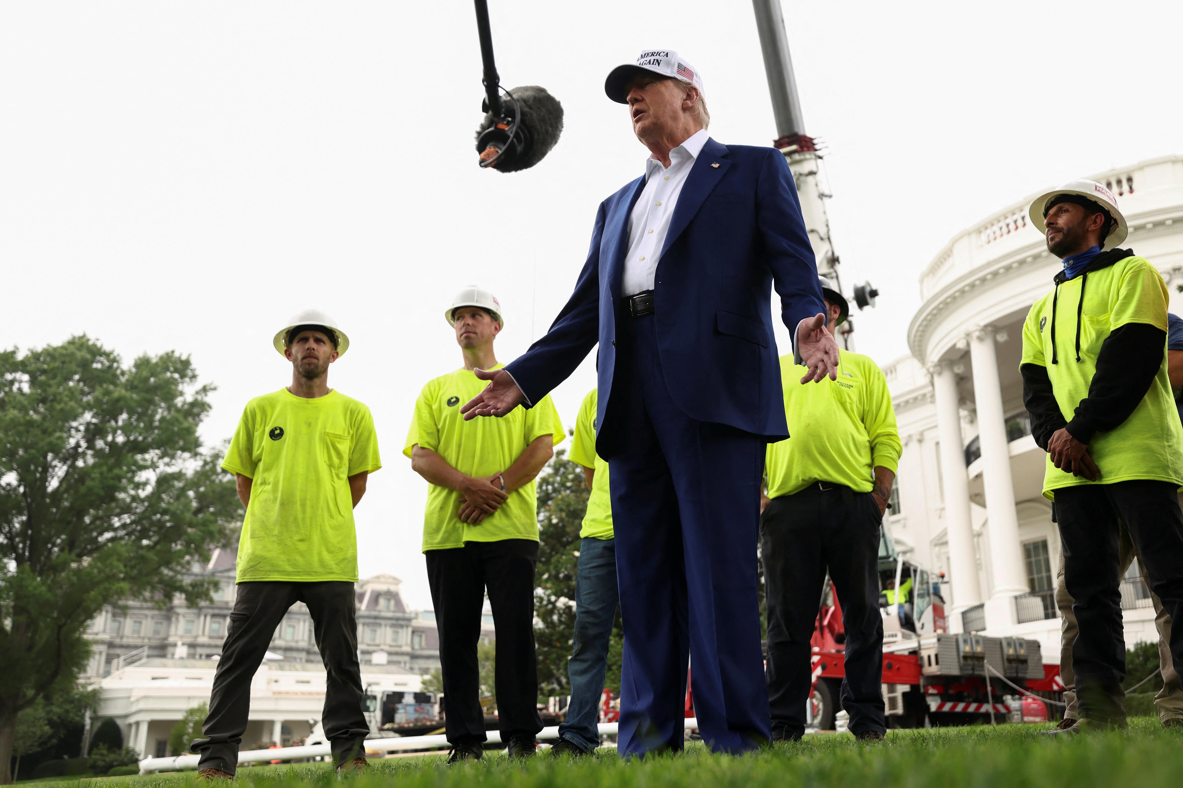 Donald Trump standing in front  of the White House with several men in high-vis standing behind him.