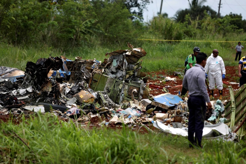 View of part of the wrecked plane, split open, with mangled, burnt debris, as people look on.