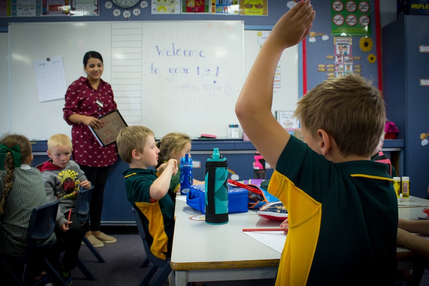 A young student raises his hand in a classroom.