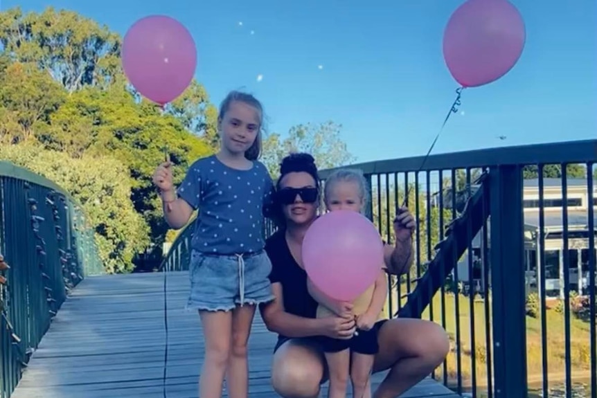 Lady with two young girls on a bridge, holding balloons