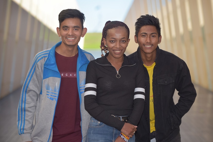 Two men and a woman are smiling at the camera with a blurred corridor behind them