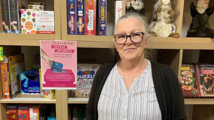 a woman with glasses and gray hair stands in front of a shelf with toys on it.
