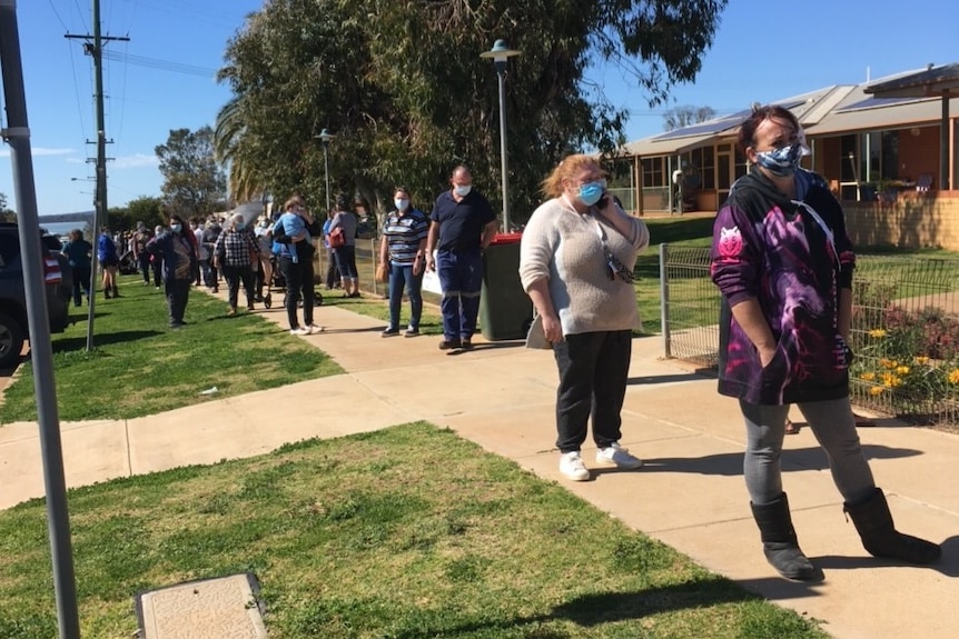 People wearing face masks, line up on a concrete footpath