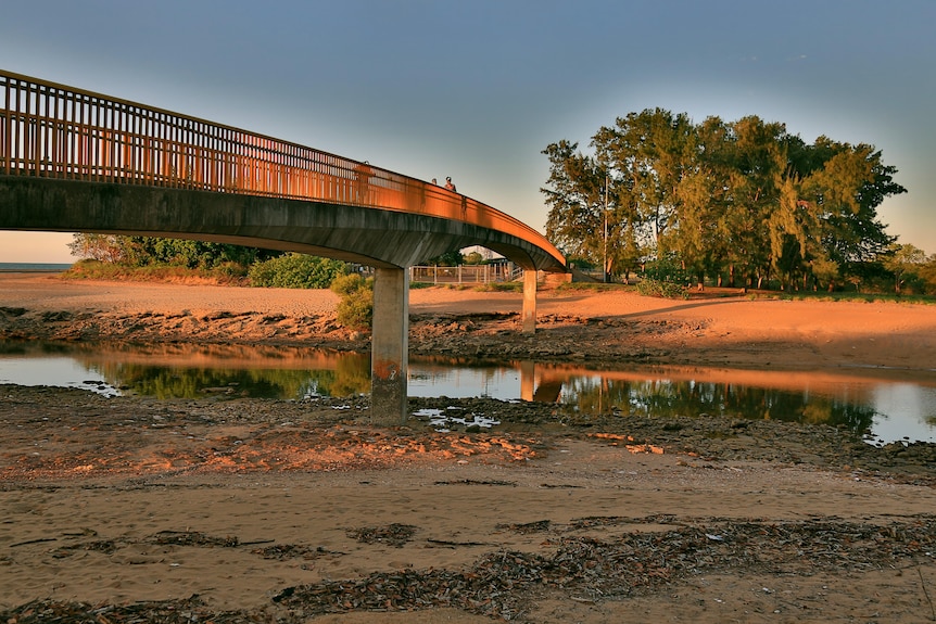Bridge over still sandy creek at low tide at sunset.