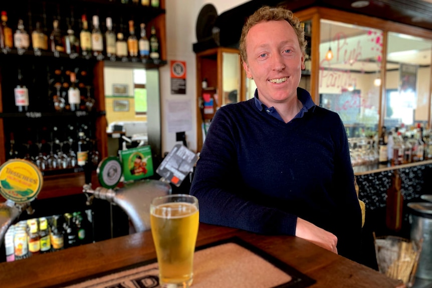 A man with a dark blue shirt standing behind a bar