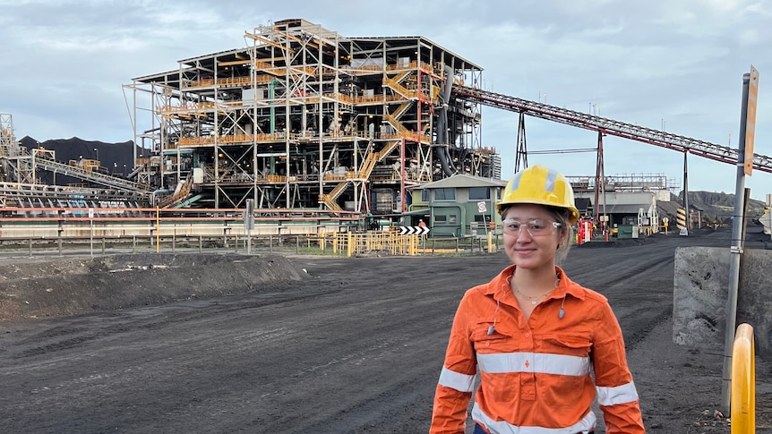 Woman stands in front of coal processing facility in dayglow and hard hat