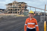 Woman stands in front of coal processing facility in dayglow and hard hat