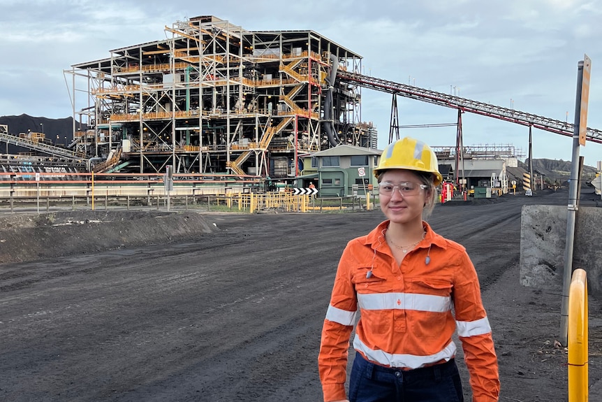 Woman stands in front of coal processing facility in dayglow and hard hat