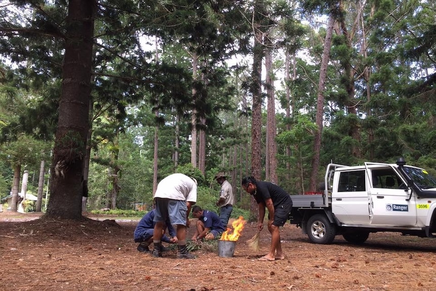 Five indigenous rangers stand around a bucket with burning leaves on Fraser Island
