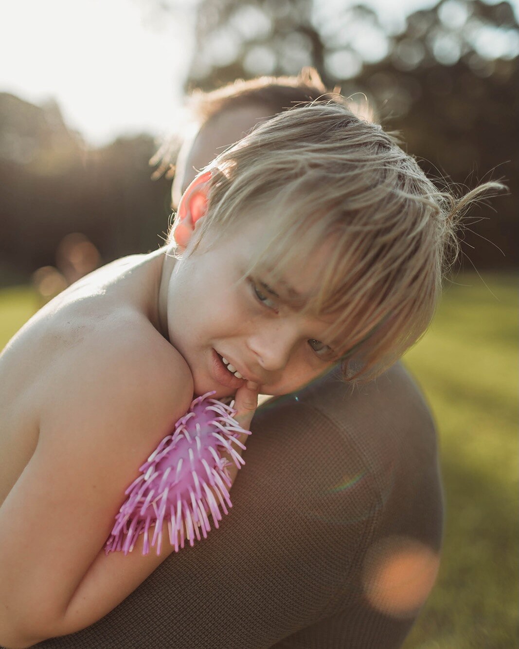 A close up photo of a young boy with blonde hair resting his head on his dad's shoulder