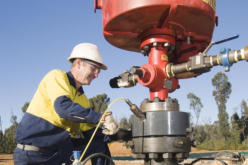A man in a navy and hi-vis yellow shirt and white hard hat adjusts equipment on a gas bore head