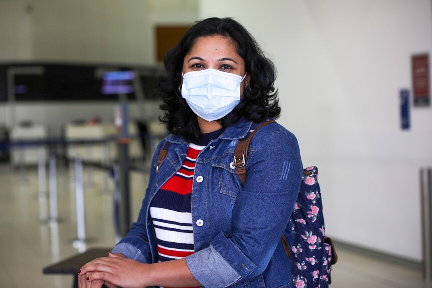 A lady with a denim jacket and a mask smiles at the camera