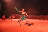 Aboriginal man in traditional dress and body paint sings and dances in the middle of a circle